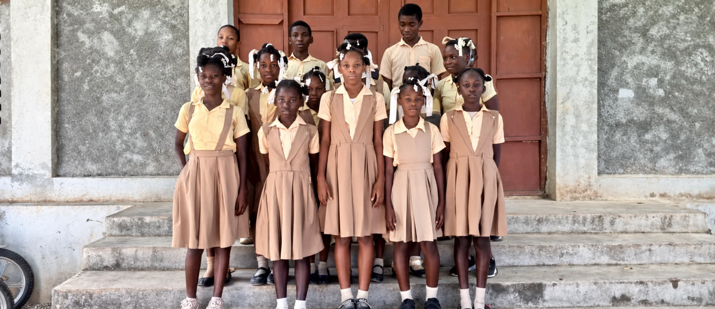 A class in tan uniforms stands on the steps of its school