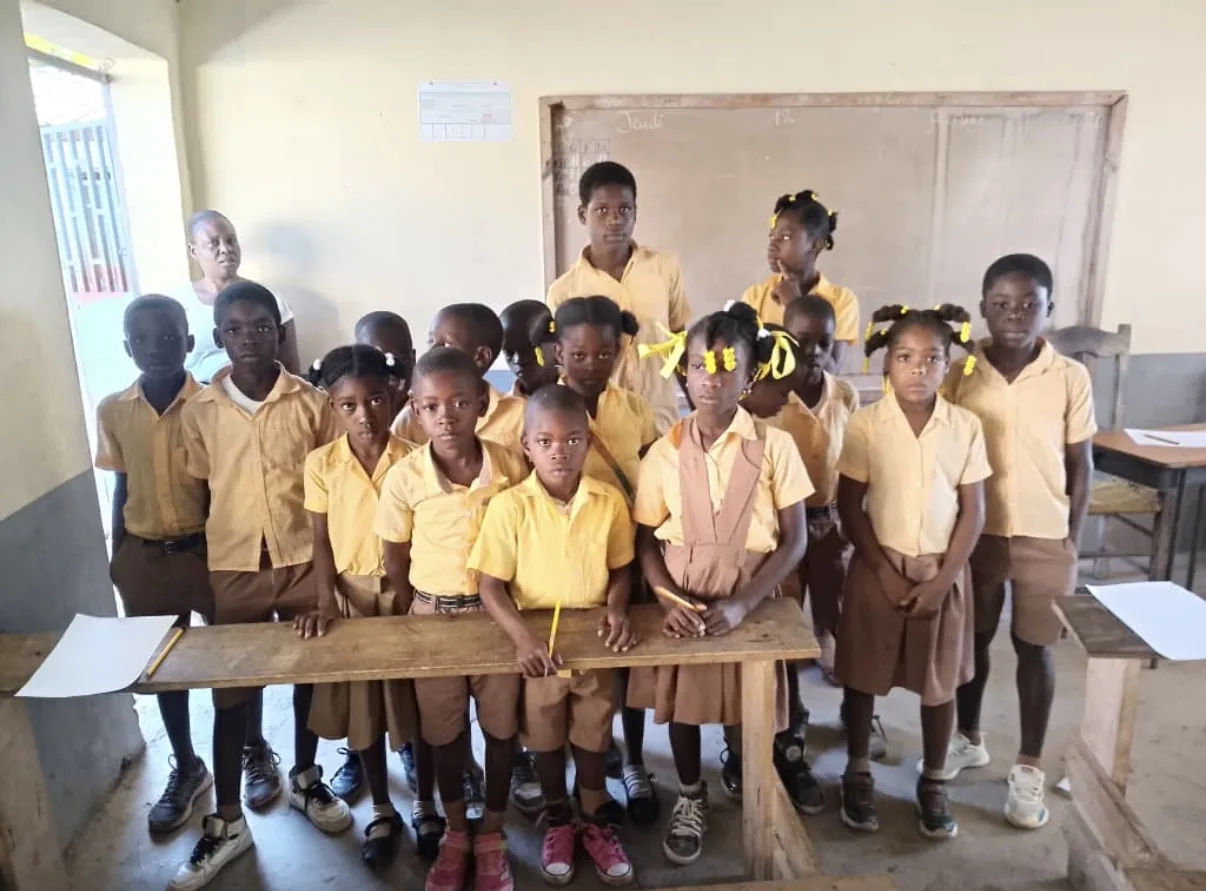 A class in yellow and tan uniforms stands at their desks
