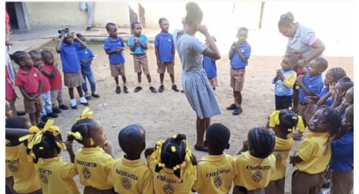 Kindergarten children in yellow shirts stand in a circle with their teachers