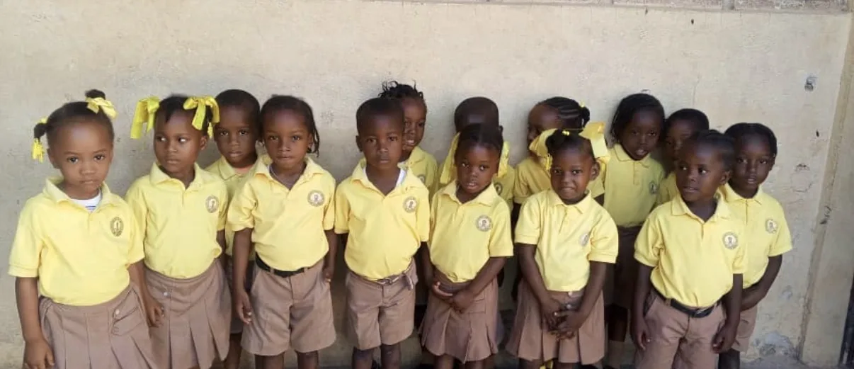 A row of young students in yellow shirts stands against a classroom wall