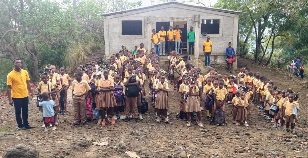 Students and teachers in yellow and tan uniforms gather in front of their small mountain school