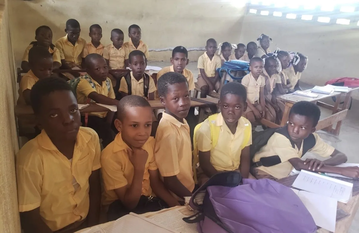 Boys in yellow shirts smile from their desks in a full HEF classroom