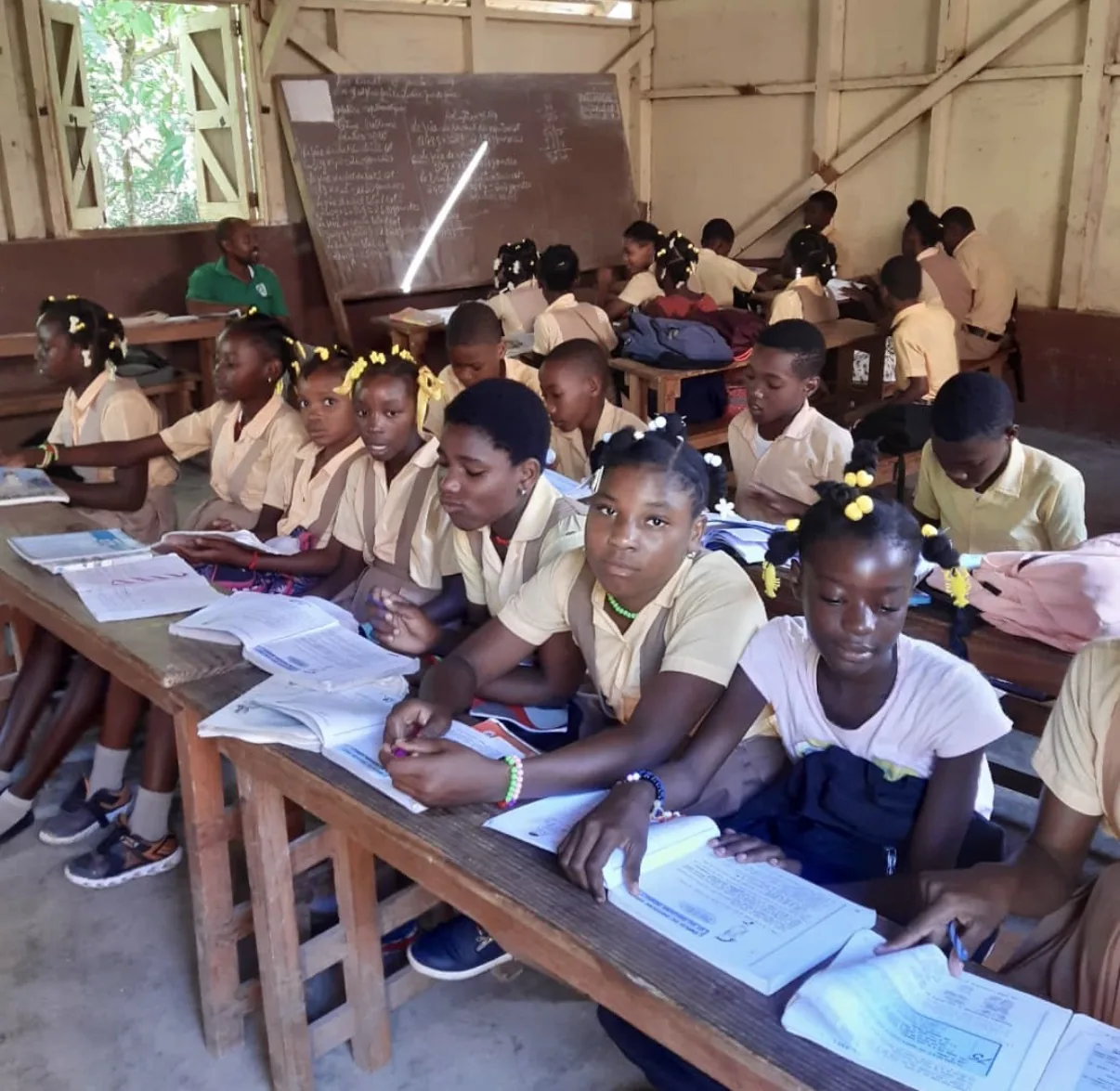 Students write in their workbooks at long wooden desks in an HEF classroom