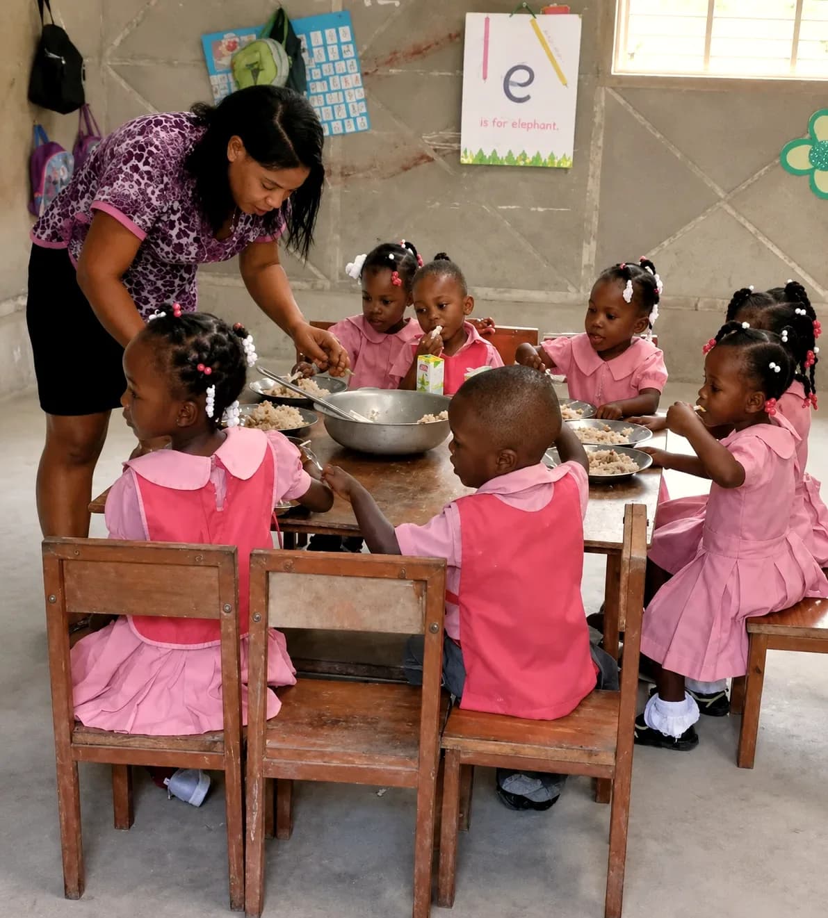 A teacher serves food to young students seated at a table at an HEF school