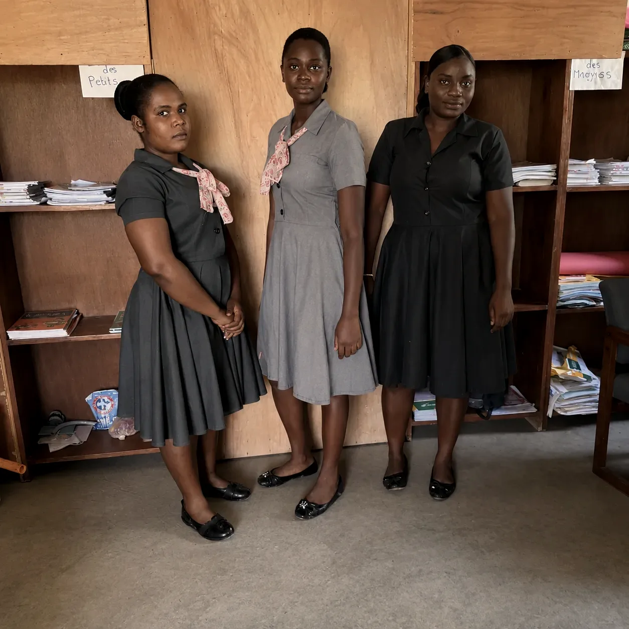 Three young women stand together in a school library at an HEF campus
